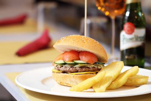 Hamburger gourmet con patatine fritte su piatto bianco. Birra e bevanda in vetro sullo sfondo.