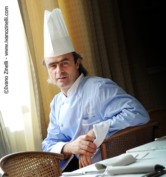 Chef Morini seduto al tavolo. Ristorante di lusso, alta cucina italiana. Cappello da cuoco.