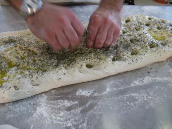 Preparazione focaccia napoletana: mani che condiscono l'impasto con erbe aromatiche e olio d'oliva. Cucina tradizionale.