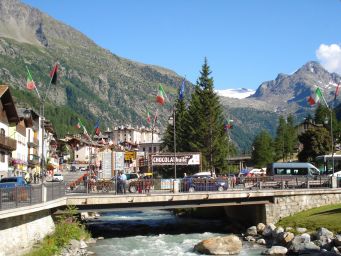 Veduta di Thuile, Valle d'Aosta. Ponte sul fiume, montagne, bandiere italiane. Paesaggio alpino.