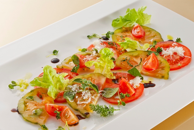 Insalata di pomodorini e caciotta De Nigris su piatto bianco. Pomodori rossi e verdi, lattuga fresca, basilico e glassa balsamica.