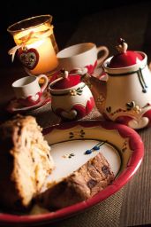 Natura morta: teiera, tazza, panettone. Ceramiche decorate, candela accesa. Atmosfera calda e accogliente.