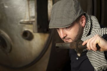 Torrefazione artigianale: uomo con coppola annusa il caffè tostato. Aroma intenso.