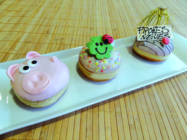 Tre krapfen decorati a tema: maiale rosa, quadrifoglio verde e Frohes Neues. Dolci di Capodanno.