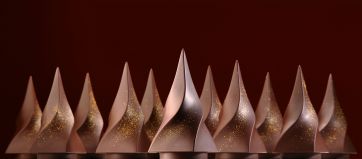 Dolci di cioccolato artistici. Eleganti dessert a forma conica, decorati con glitter dorati. Pasticceria di lusso.