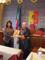 Chef Matteo Bertacchi riceve premio gastronomico. Bandiere italiane e stemma comunale sullo sfondo.