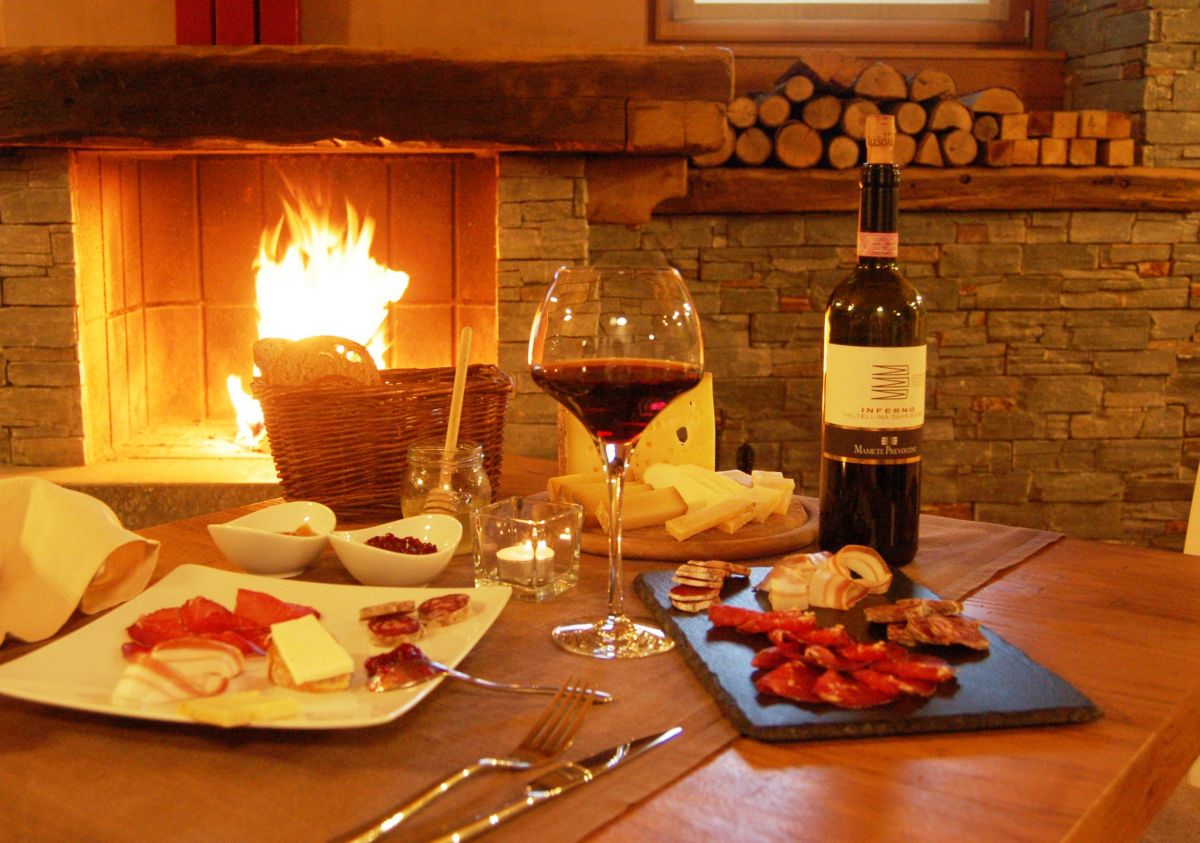 Stube con vino rosso, formaggi e salumi. Camino acceso. Atmosfera accogliente.