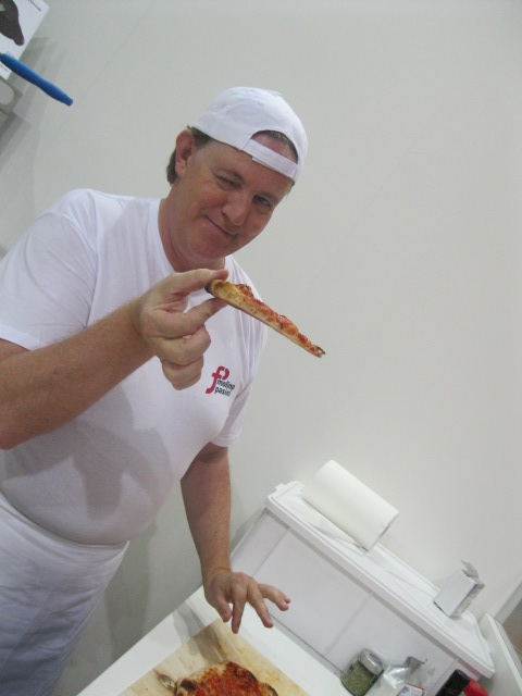 Pizzaiolo ammiccante mostra fetta di pizza. Cucina italiana, pizza fatta in casa.