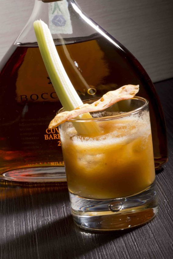 Cocktail artigianale con sedano e liquore. Drink rinfrescante, ideale per aperitivo. Bottiglia di liquore sullo sfondo.