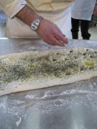 Focaccia fatta in casa. Mani di cuoco che preparano focaccia con erbe e olio d'oliva. Cucina tradizionale italiana.