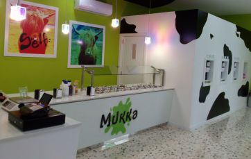 Interno negozio Mukka: bancone bianco, macchie mucca, distributori gelato. Design moderno e originale.