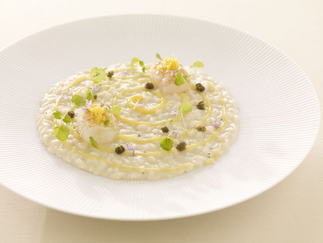 Risotto gourmet con scampi, limone, capperi e rosmarino. Piatto di riso italiano, cucina raffinata.