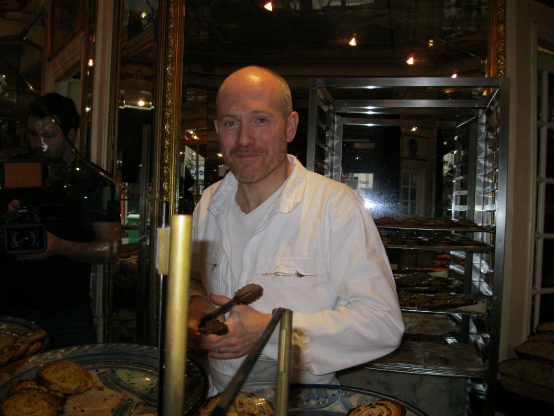 Panettiere con pinze in pasticceria. Dolci da forno su vassoi e scaffali.