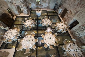 Interno di location per eventi con tavoli rotondi apparecchiati su pavimento in vetro. Matrimonio, ricevimento.