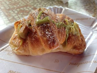 Brioche al pistacchio su piatto. Cornetto farcito con crema di pistacchio e zucchero a velo. Colazione dolce.