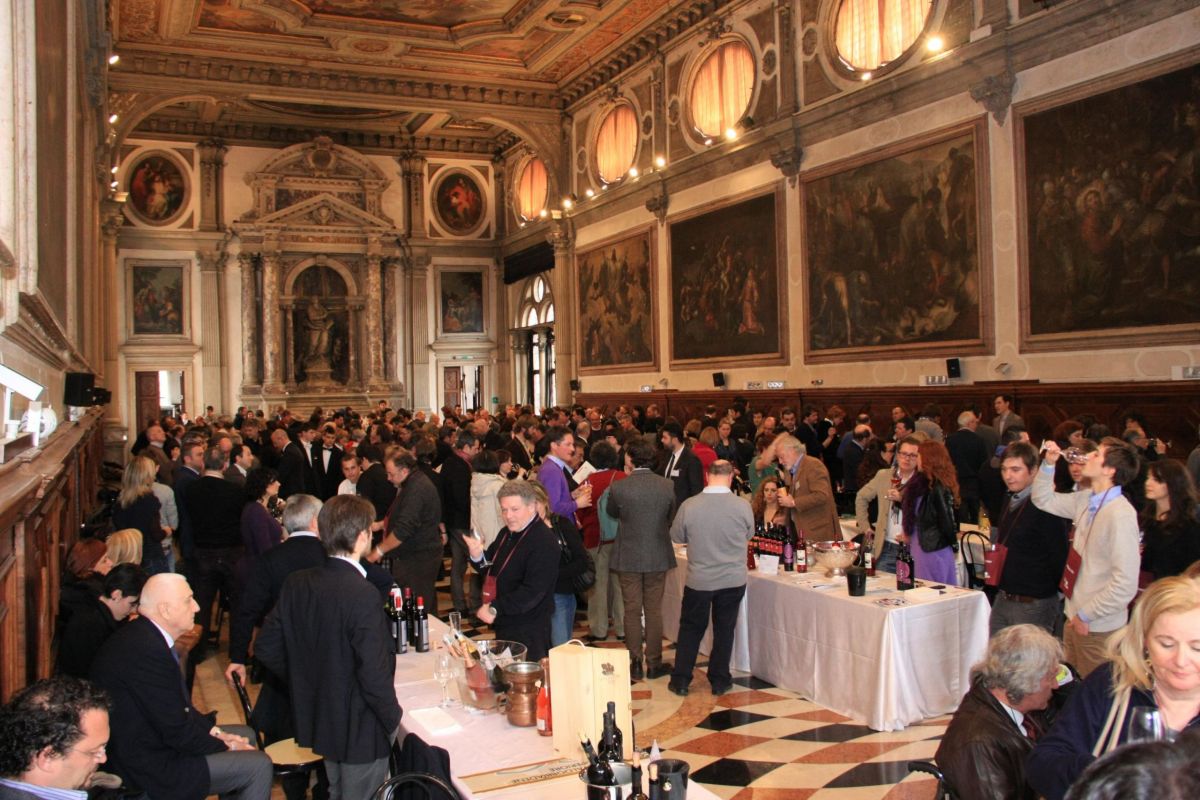 Degustazione vini in sala storica. Persone, tavoli con bottiglie, dipinti. Evento enologico.