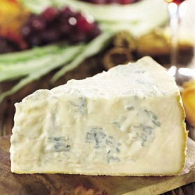 Primo piano di gorgonzola DOP, formaggio erborinato italiano su tagliere di legno.