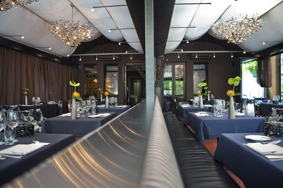 Interno elegante di ristorante. Tavoli apparecchiati, lampadari moderni, atmosfera raffinata.