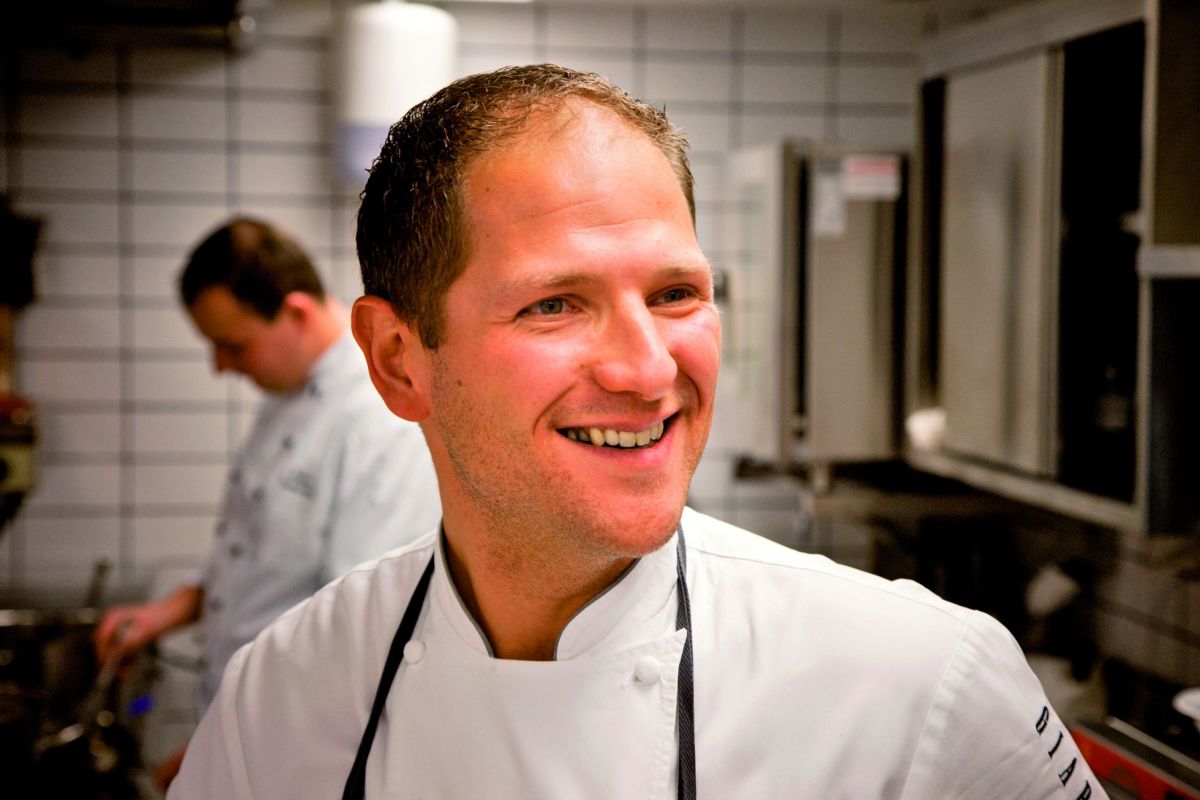 Chef sorridente in cucina professionale. Abbigliamento da cuoco, ambiente di lavoro. Ristorazione di qualità.