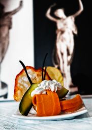 Piatto gourmet con frutta, verdura e panna. Sculture di danzatrici sullo sfondo.