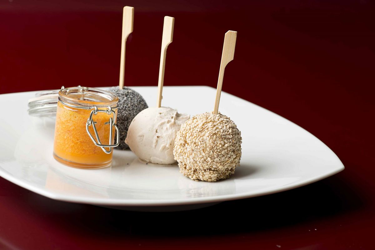 Dolci sfiziosi su piatto: palline con sesamo, papavero e crema di frutta in vasetto. Delizie culinarie.