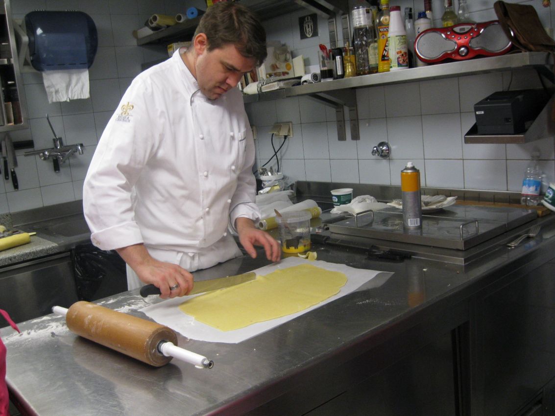 Chef taglia pasta fresca in cucina professionale. Mattarello e piano in acciaio.