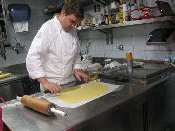 Chef taglia pasta fresca in cucina professionale. Mattarello e piano in acciaio.