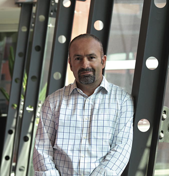 Ritratto di uomo con barba. Camicia a quadri, appoggiato a struttura metallica. Look professionale.