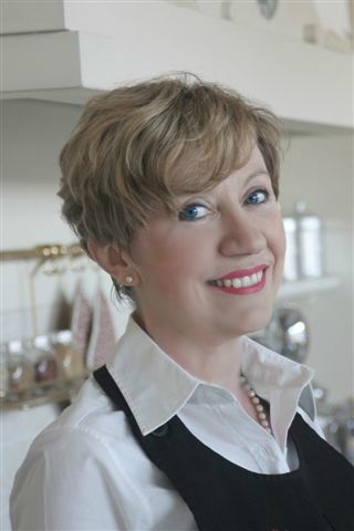 Ritratto di Elisabetta Arcari, chef sorridente con capelli biondi e grembiule nero. Cucina italiana, food blogger.