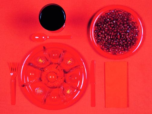 Natura morta rossa: melograno, pomodori, posate, tovagliolo e bevanda scura. Concetto di cibo e colore.