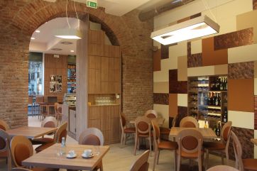 Interni di ristorante: tavoli in legno, sedie design, parete decorativa e archi in mattoni. Arredamento accogliente.
