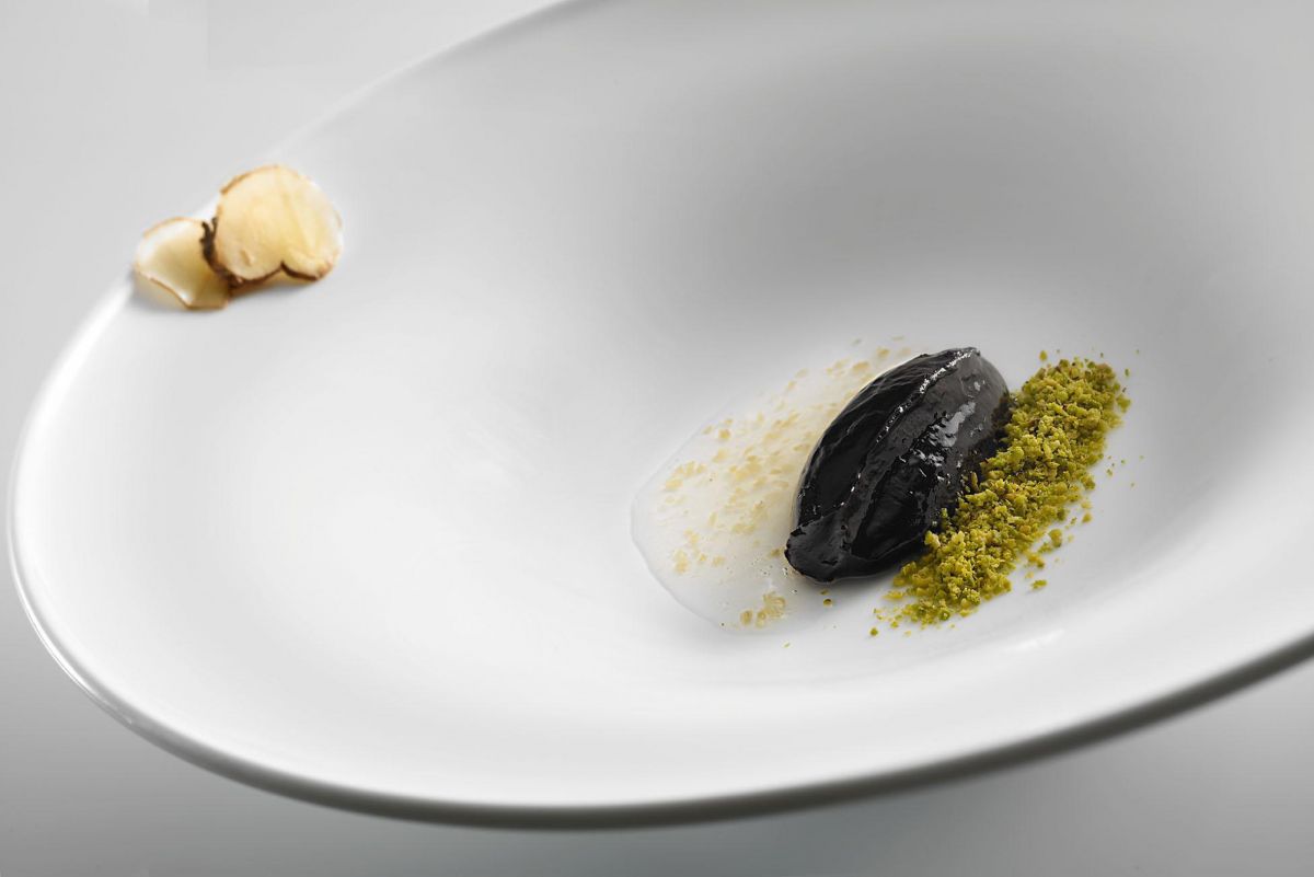 Dessert gourmet su piatto bianco: gelato nero, pistacchio, salsa chiara e tartufo.