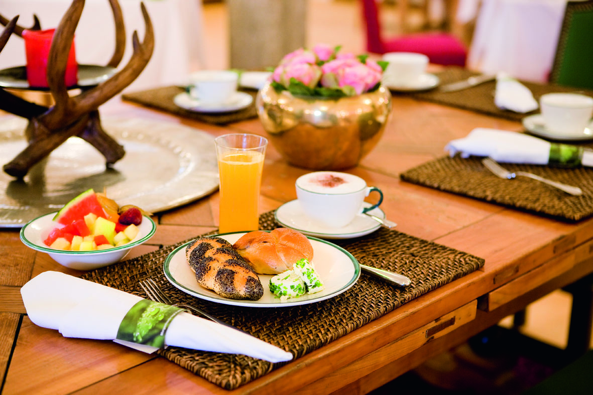 Colazione austriaca su tavolo in legno: pane, frutta fresca, succo d'arancia e cappuccino. Atmosfera accogliente.