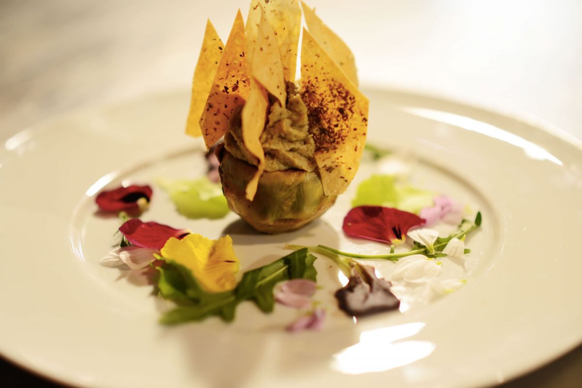 Carciofo ripieno con crema di carciofi e chips, decorato con fiori eduli. Cucina gourmet, piatto elegante.