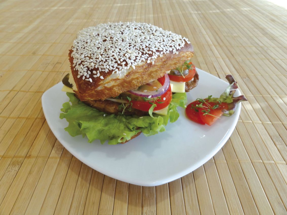 Gustoso burger gourmet su piatto bianco. Panino con sesamo, lattuga, pomodoro, cipolla e formaggio.