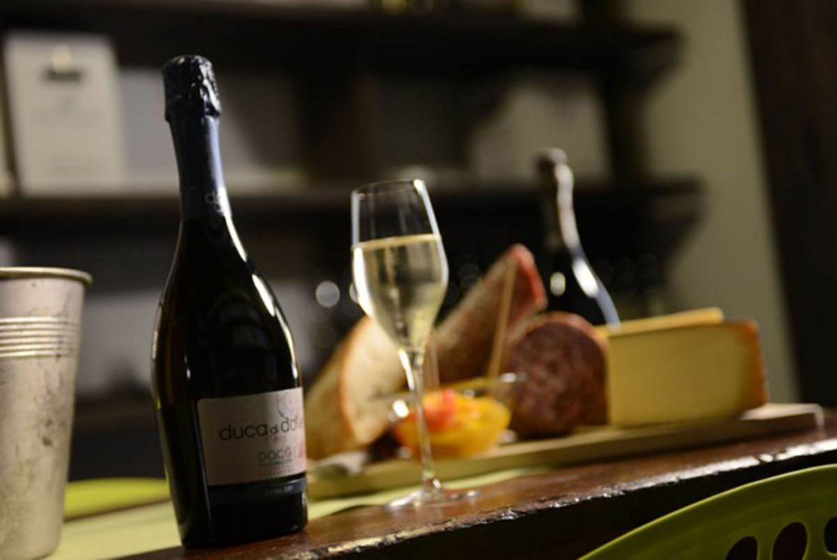 Natura morta con vino, formaggio e salumi. Bottiglia di vino Duca di Dolle e calice.