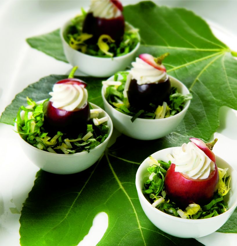 Acini d'uva farciti con crema, serviti in ciotole su foglie di fico. Antipasto gourmet, cucina creativa.