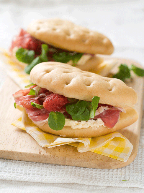 Focaccia farcita con prosciutto, formaggio e insalata. Panino gourmet, cucina italiana.
