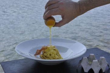 Carbonara gourmet: uovo versato su spaghetti con guanciale croccante. Ricetta italiana.