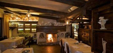 Interni rustici del ristorante: travi in legno, camino acceso e tavoli apparecchiati. Atmosfera accogliente.