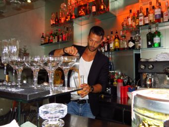 Barman prepara cocktail. Bottiglie di liquori sullo sfondo. Barman al lavoro, bicchieri da cocktail.