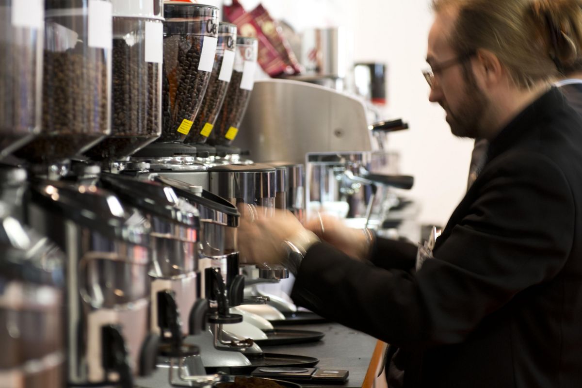 Barista al lavoro con macchina da caffè professionale. Grani di caffè in contenitori. Esperienza TriestEspresso Expo.