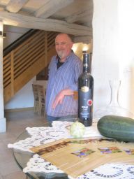 Uomo con bottiglia di vino rosso Miraz, melone e brochure. Degustazione vini e prodotti tipici.