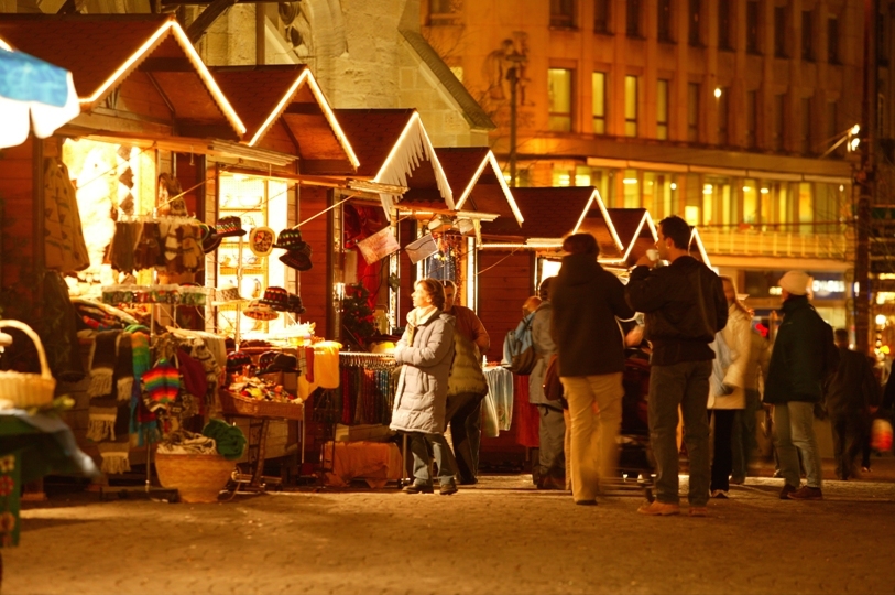 Mercatino di Natale illuminato. Bancarelle di legno con luci e persone. Artigianato natalizio in vendita.