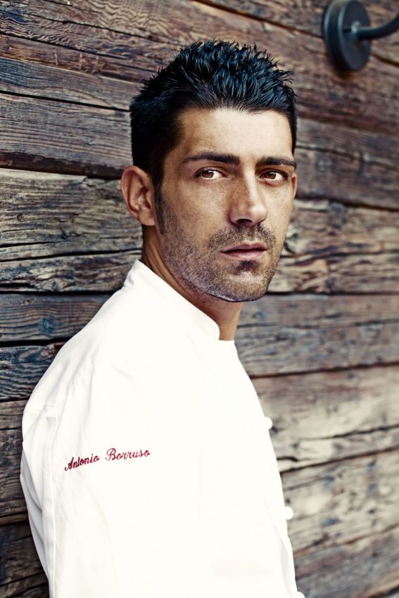 Ritratto dello chef Antonio Borruso in divisa bianca su sfondo di legno rustico. Cucina italiana di alta qualità.