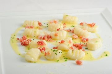 Gnocchi di patate allo speck su piatto bianco. Ricetta tradizionale italiana.