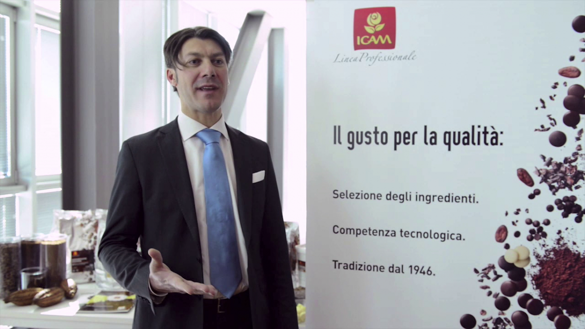Uomo in giacca e cravatta con banner ICAM. Qualità e tradizione dal 1946 per cioccolato e cacao professionali.