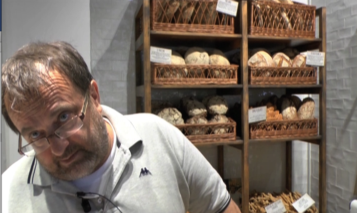 Uomo con pane artigianale. Scaffale di legno con cesti di pane fresco in panetteria. Prodotti da forno di alta qualità.
