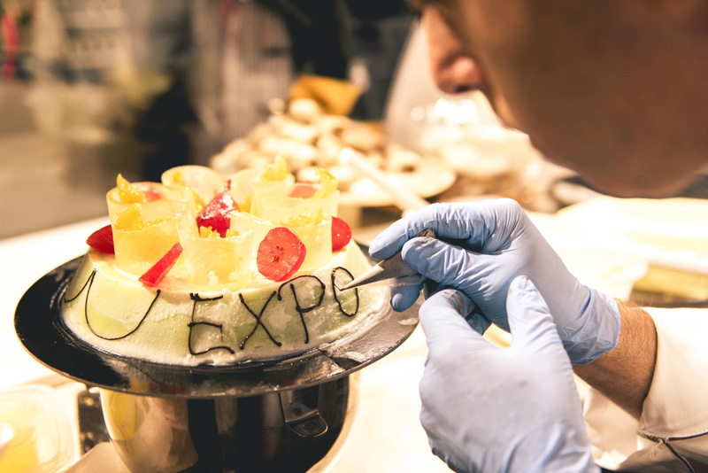 Chef decora torta EXPO. Pasticceria artigianale con frutta fresca. Dolce goloso, evento speciale.