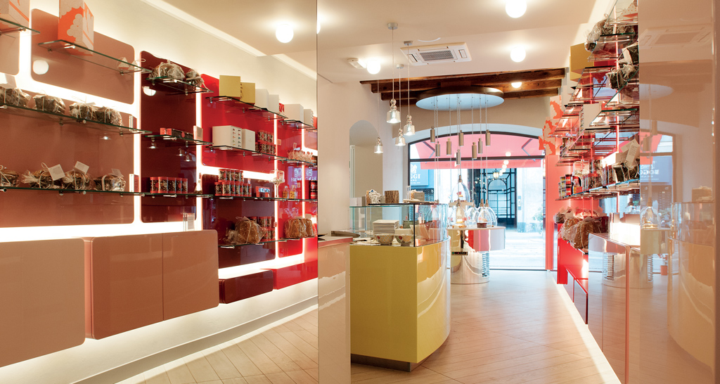 Interno negozio di dolciumi. Scaffali rossi con prodotti, bancone giallo. Design moderno e illuminazione curata.